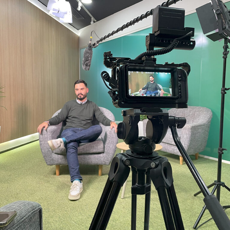 Gravação de entrevista em vídeo com homem sentado em poltrona, câmera profissional e microfone boom em estúdio