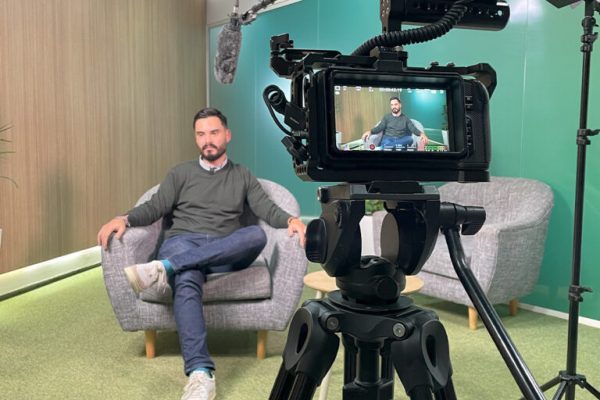 Gravação de entrevista em vídeo com homem sentado em poltrona, câmera profissional e microfone boom em estúdio
